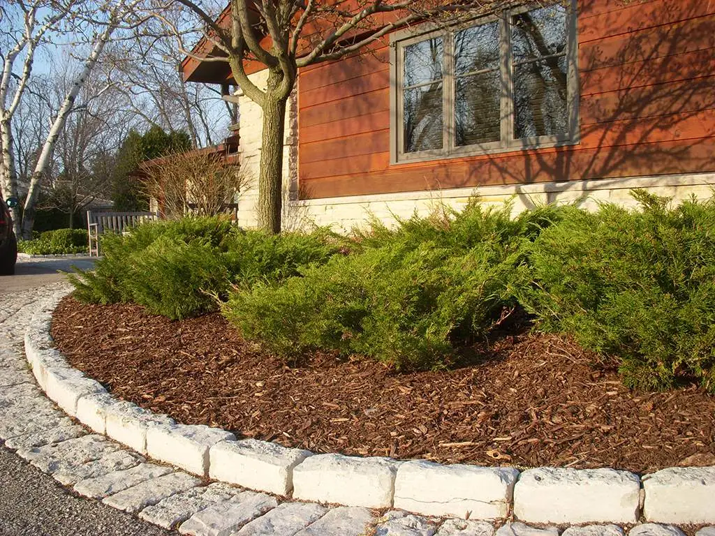 A curved bark bed with a paver edge in front of a house